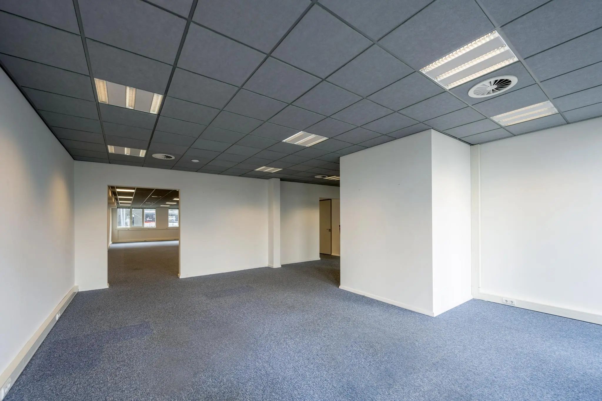 Lege kantoorruimte aan de De Ruijterkade met systeemplafond, blauwe vloerbedekking en witte muren.